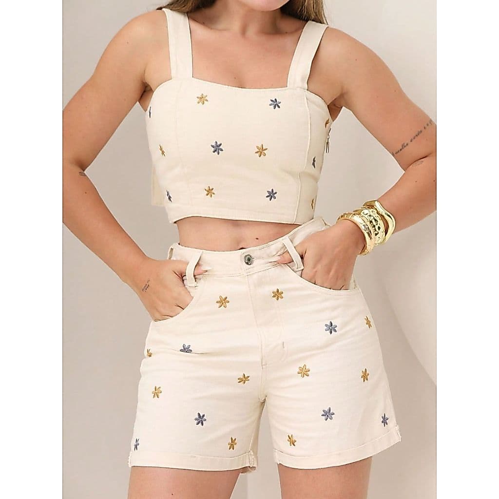 Conjunto feminino de duas peças em jeans com bordado floral sem mangas, composto por blusa cropped e shorts curtos.