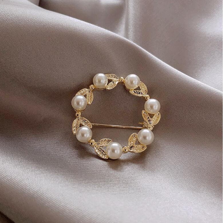 Broche circular com folha de pérola para fixar acessórios de vestuário.
